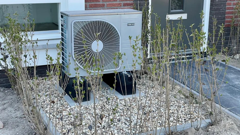 Eine Wärmepumpe steht vor einem Haus auf einem Rasenstück. 